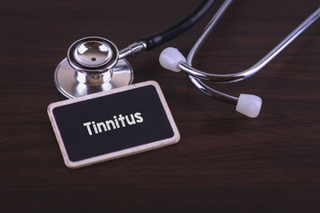 Medical Concept- Tinnitus words written on label tag with Stetoscope on wooden background