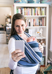 Mother with son in sling taking selfie with smartphone
