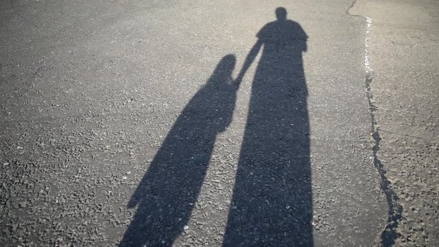 Long shadow of parent and child walking along road together holding hands