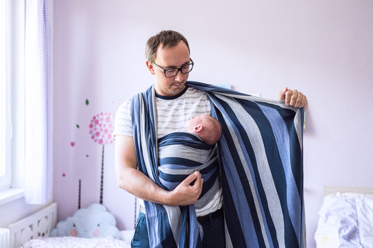 Young father wrapping his newborn baby son into sling