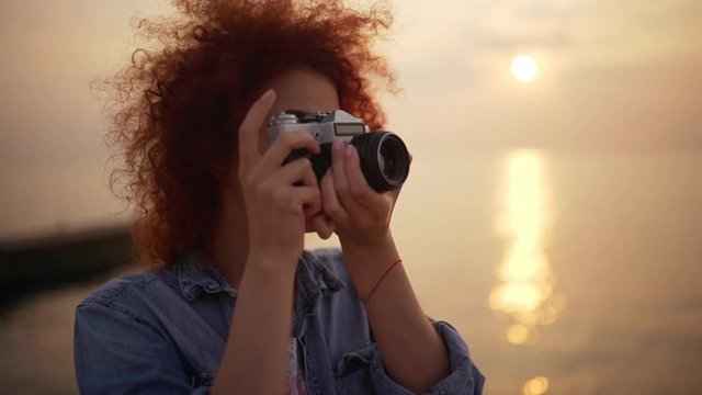 Beautiful redhead girl taking photo at sunrise seashore Slow motion