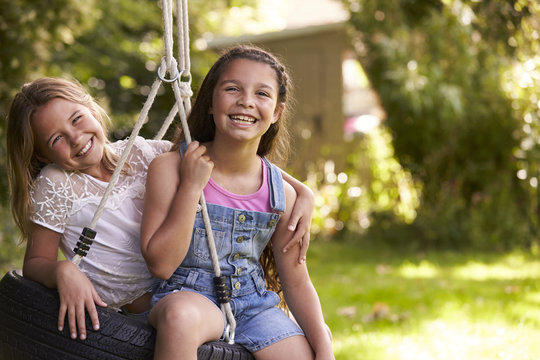 Portrait Of Two Girls Playing On Tire Swing In Garden