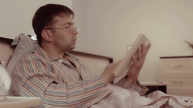 Young handsome man looking through his book before going to sleep
