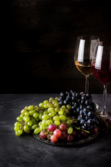 Wine in glasses and different types of grape on dark background.