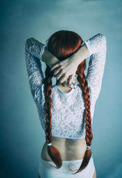Chica joven pelirroja en ropa interior con el pelo recogido en dos trenzas de espaldas a la c&aacute;mara 