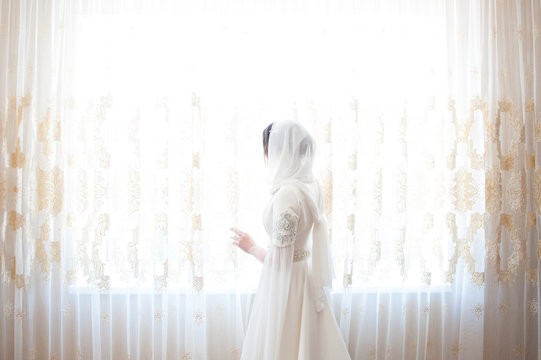 muslim woman in a white headscarf standing at the window
