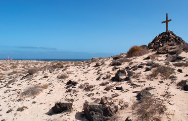 Fuerteventura, Isole Canarie: una croce di legno su una pila di sassi e il faro del Toston, vicino al villaggio di pescatori di El Cotillo, il 3 settembre 2016