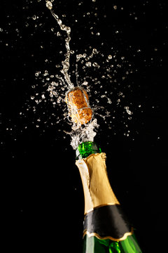 Green champagne bottle with gold foil and cork explosion