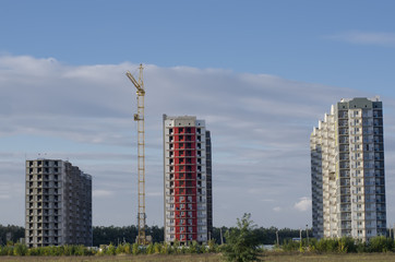 Fototapeta na wymiar Three buildings and a construction crane in the open field.