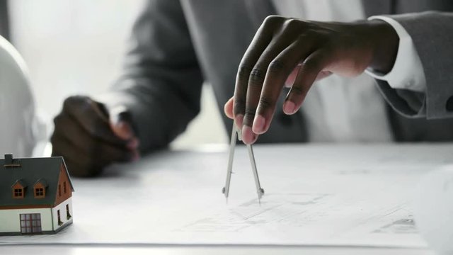 Young black architect working on construction blueprint in white office, he draws with a divider and ruler. Slow motion
