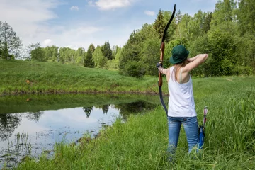 Zelfklevend Fotobehang female archer aiming at a target outdoors © Mikhail Apukhtin