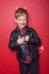 Little handsome devil with horns and tail. Kid. Halloween. Studio portrait isolated over red background