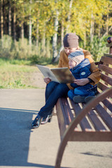 Young woman and little boy sitting on the bench in autumn Park and reading book. Family enjoying time together. Mother teaches son