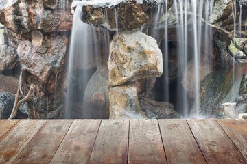 wooden floor and nature background soft waterfall flowing over a stone in the garden