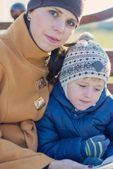 Young woman and little boy sitting on the bench in autumn Park and reading book. Family enjoying time together. Mother teaches son