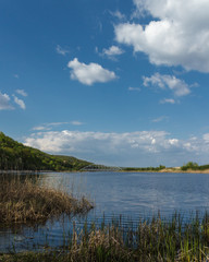 A beautiful Blue Lake with yellow grass in the foreground and a blue sky with clouds