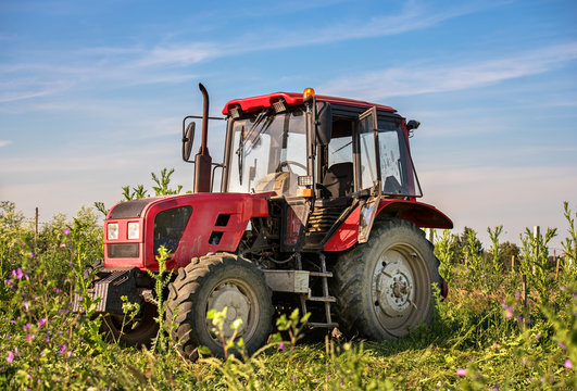 A stationary red tractor is parked on the edge of a field of bar