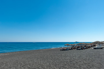 Fototapeta premium The people sunbathing on the black beach of Kamari in Santorini, Greece.