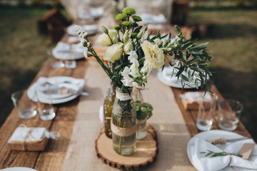 The composition of flowers and greenery standing on served table in the area of wedding party
