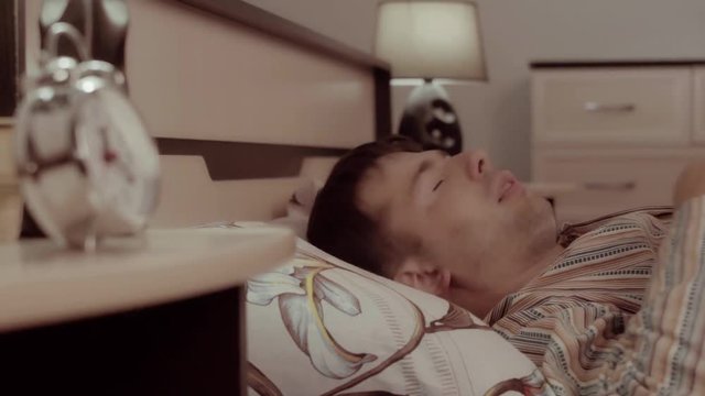 Young fair-skinned man sleeping in his bed has a nightmare which makes him turn