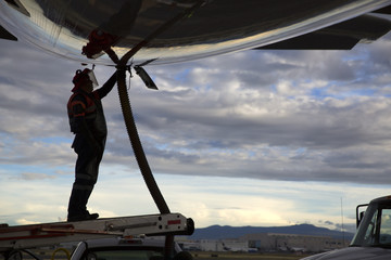 Airport staff operator refueling aircraft against blue sky