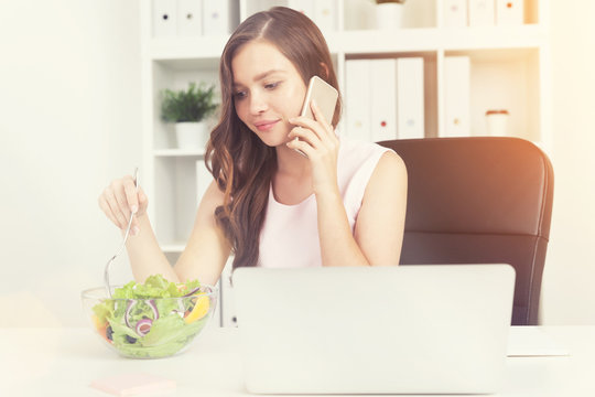 Woman with laptop eating salad in sunit office