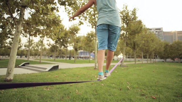 Guy walks on slackline at public park