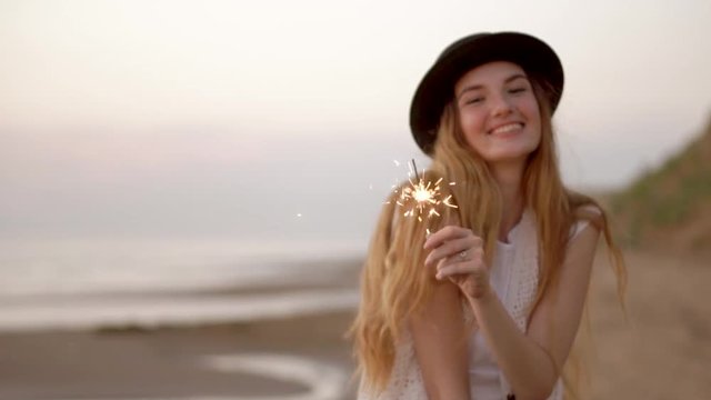 Teenage beautiful girl with sparklers on the beach at sunset HD slow motion