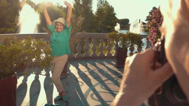 Senior lady with raised arms. Man's hand holding camera. Feel young and free. Photographer and the model.