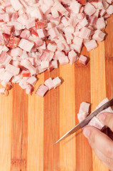 Bacon being cut with steel knife by a chef on a cutting board meat.