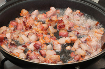 Frying bacon pieces in a pan with hot oil. Preparing ingredients to make a dish. Bacon roasted in pan with hot oil.