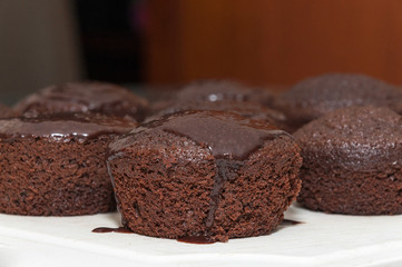 Small chocolate cakes with dripping chocolate icing on top. Homemade cakes made in round shape in a row.