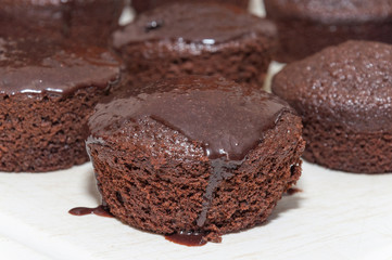 Small chocolate cakes with dripping chocolate icing on top. Homemade cakes made in round shape in a row.