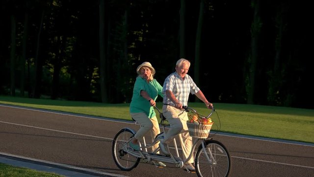 Senior couple riding tandem bike. People ride on the road. Spin the pedals faster. Race with the time.