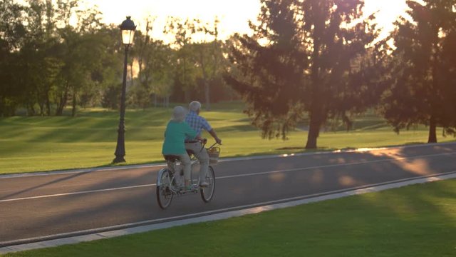 Senior couple riding tandem bicycle. Two people on a bike. Follow the sun. Picking up speed.