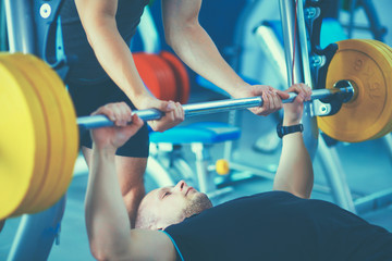 Young man lifting the barbell in gym with instructor