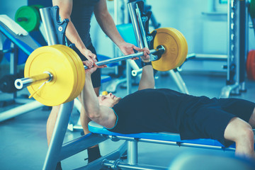 Obraz premium Young man lifting the barbell in gym with instructor
