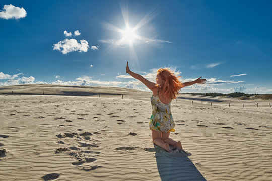 Happy Redheaded woman waving hands among Leba dunes Desert
