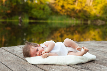 Obraz na płótnie Canvas Baby lying on the blanket on pier hext to the river