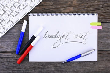 Notebook with Budget Cuts Handwritten on wooden background 