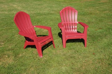 Two red Adirondack chairs in the grass