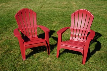 Two red Adirondack chairs in the grass