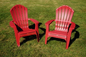 Two red Adirondack chairs in the grass