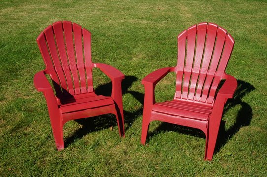Two Red Adirondack Chairs In The Grass
