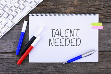 Notebook with TALENT NEEDED Handwritten on wooden background and modern keyboard
