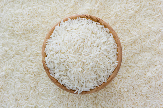 grains of Thai jasmine rice in wooden bowl on white rice background, top view with copy space, high resolution product.