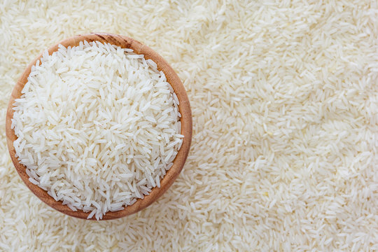 grains of Thai jasmine rice in wooden bowl on white rice background, top view with copy space, high resolution product.