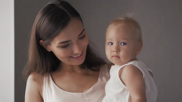 Young Happy Mother Holding her Newborn Child. Family at home. Beautiful smiling Mom and Happy Baby Together.