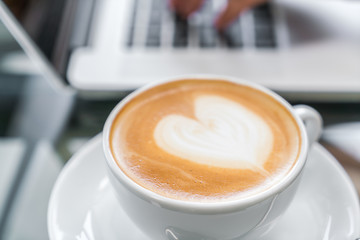 Closeup of  Latte Coffee art and woman hand typing on laptop key