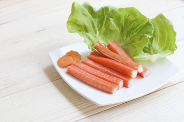 Kanikama, Crab stick with green vegetable on white plate (on wooden table background), Front view and close up.